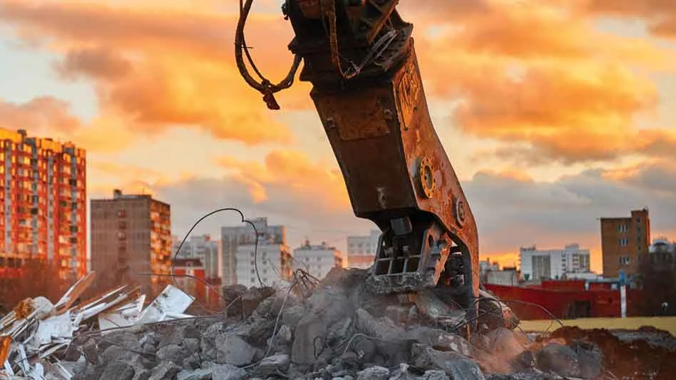 excavator grabs concrete in an urban setting at sunset